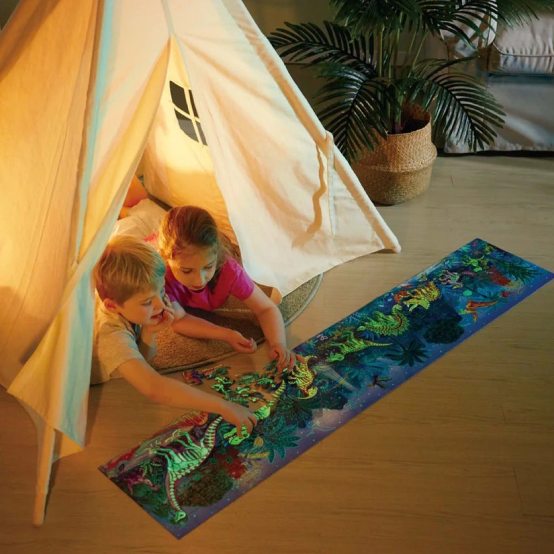 A boy and girls playing inside a tee pee tent indoors at night doing a large panoramic glow in the dark dinosaur puzzle from Hape